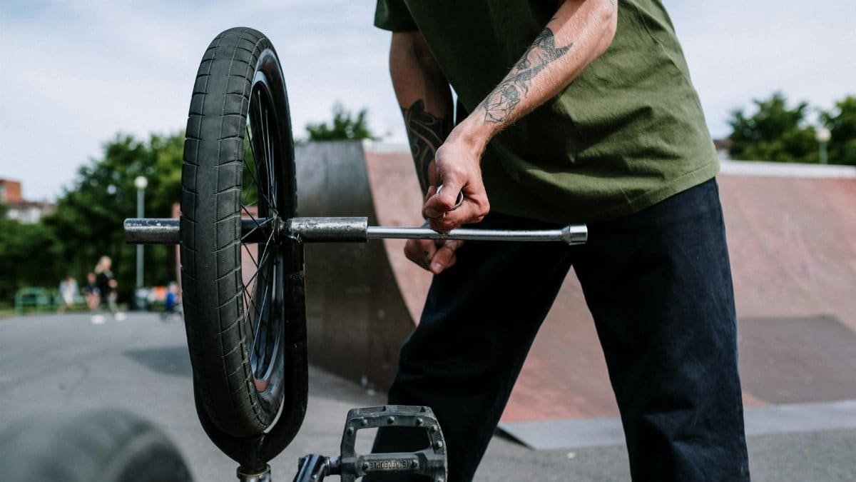 A BMX cyclist skillfully fixes their bike outdoors, focusing on wheel maintenance.