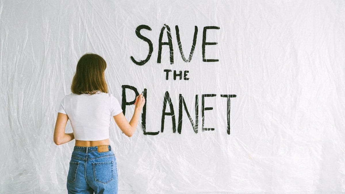 Back view of a woman with brown hair writing 'Save the Planet' on a white background with a plastic sheet.