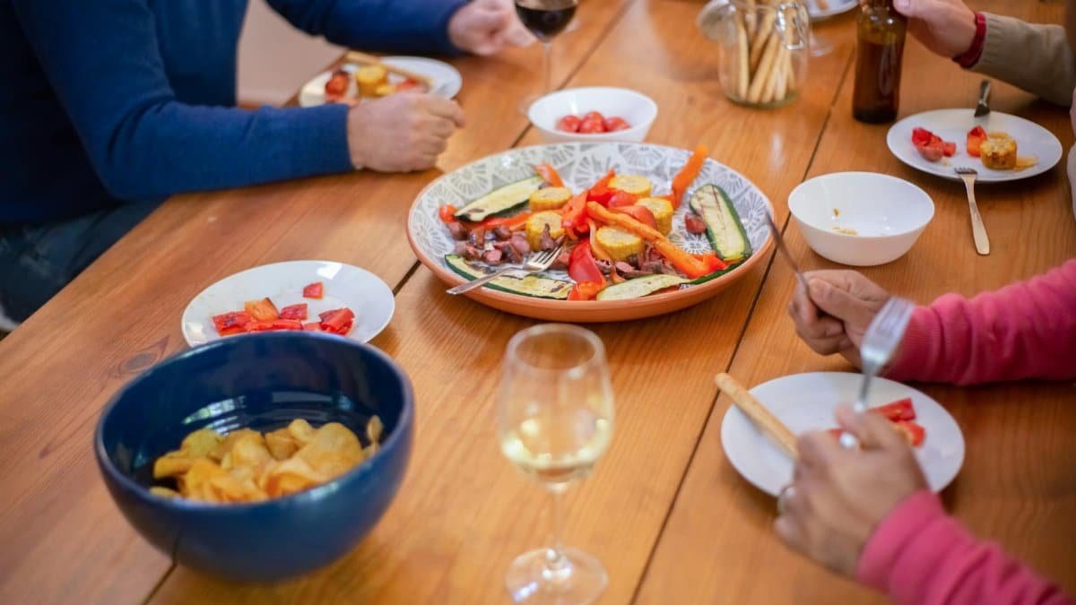 Casual dinner party with friends sharing food and drinks around a wooden table.