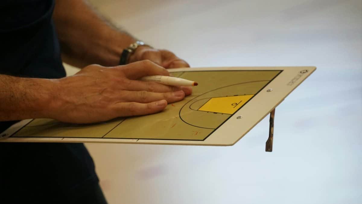 Close-up of a coach using a basketball tactics board to plan game strategy indoors.