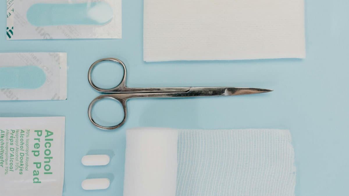 Top view of various medical supplies including scissors, bandages, and prep pads on a blue surface.