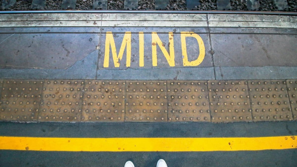 Close-up of railway platform edge with 'MIND' warning and yellow safety line, England.