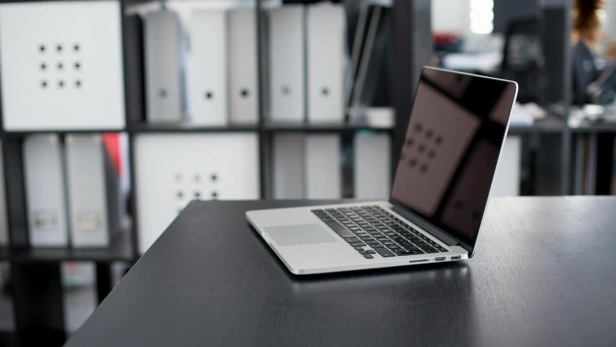 MacBook Pro displayed on a minimalist office desk with shelves in the background.