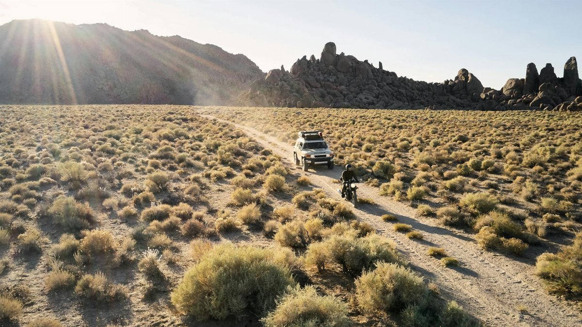 From above view of narrow road in dry highland valley with jeep and motorbike under bright evening sun