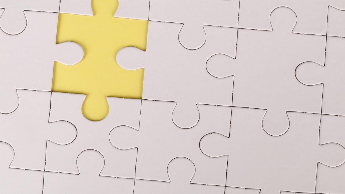 Close-up of a white jigsaw puzzle with a single yellow piece missing, symbolizing incompleteness.