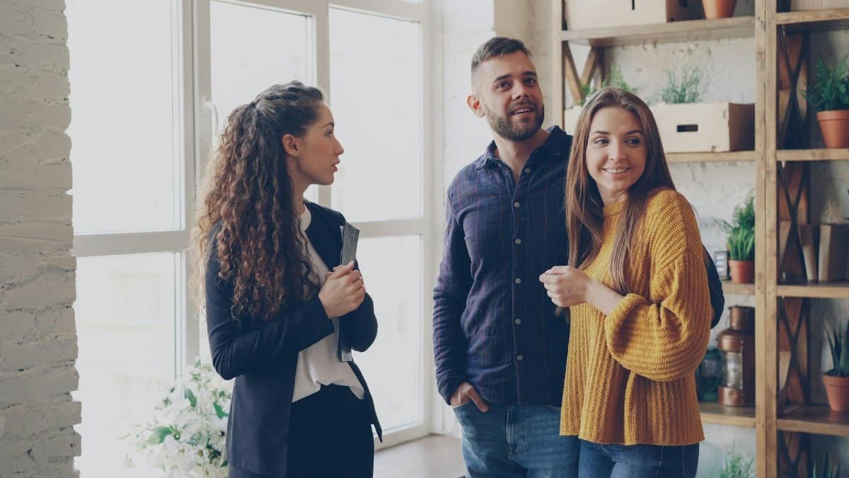 Real estate agent presenting an apartment to a smiling couple in a cozy modern setting.