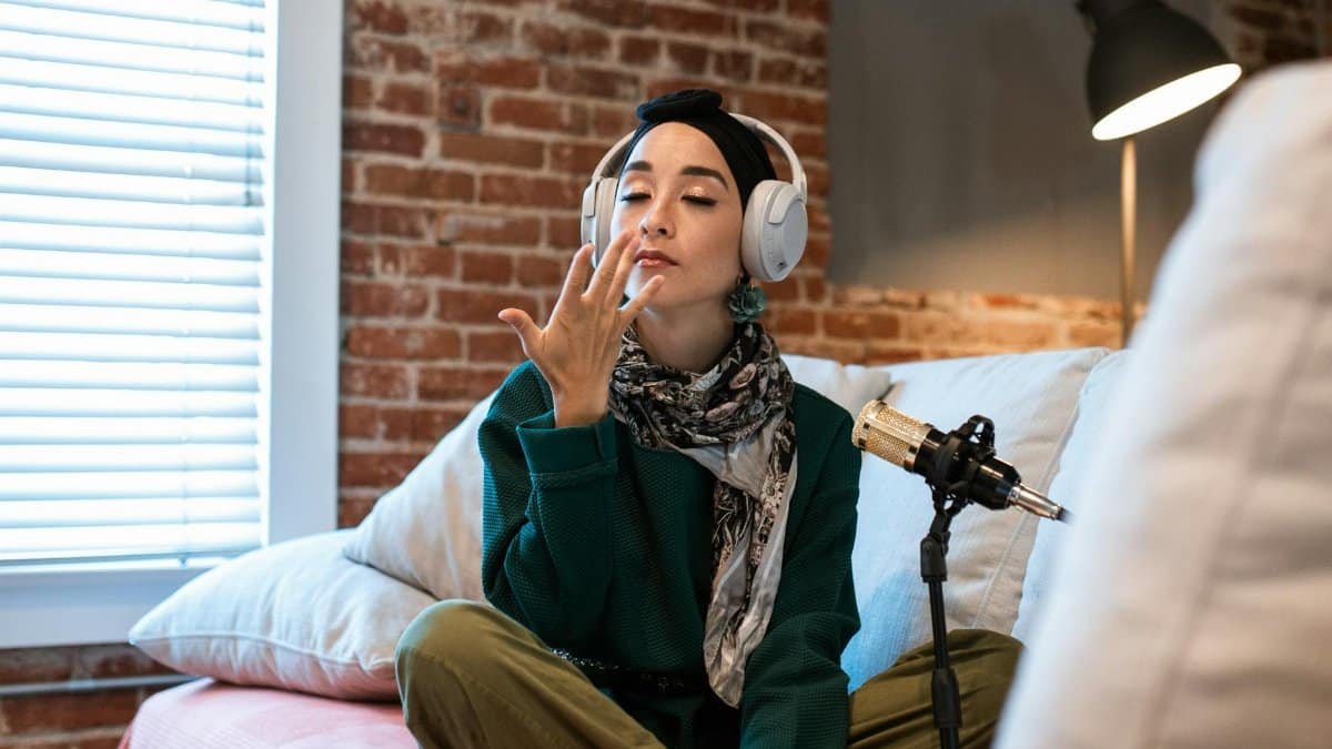 A young woman podcasting with microphone and headphones in a cozy home setup.