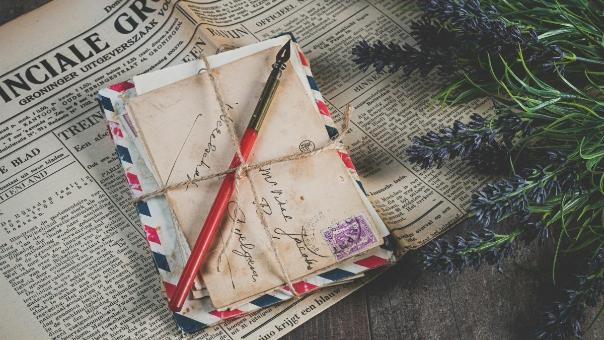 Old handwritten letters with vintage stamps and lavender on a newspaper background.