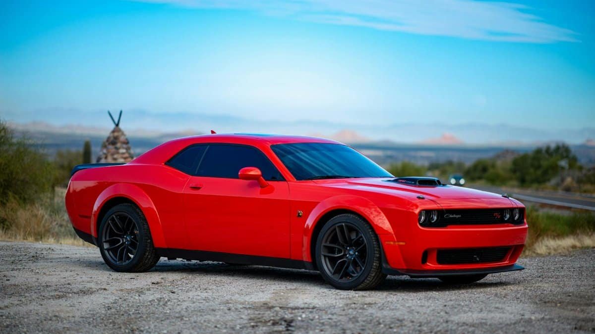 Red Dodge Challenger muscle car parked in a scenic Arizona landscape with clear blue skies.