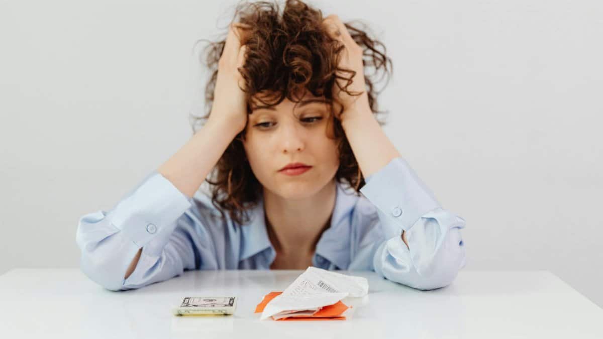 Woman in blue sleeves appears stressed while looking at receipts and money, symbolizing financial stress.