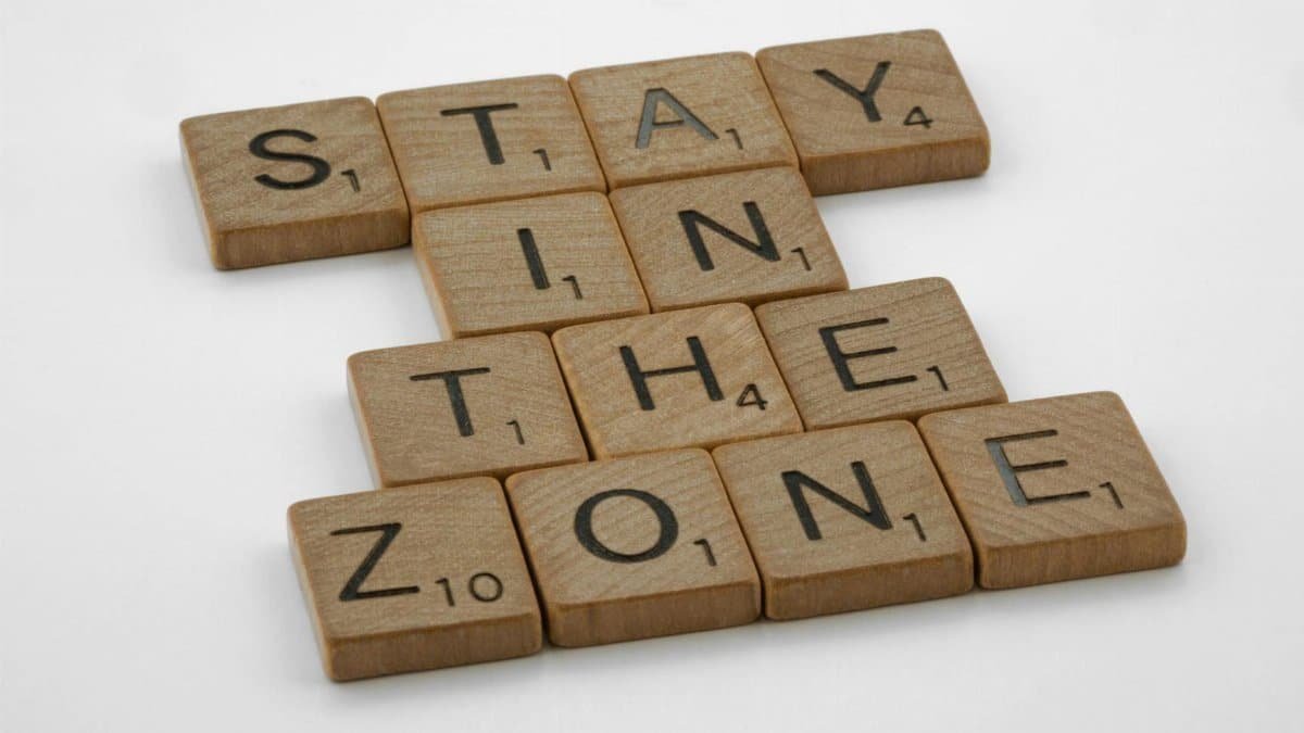 Wooden Scrabble tiles arranged to spell 'Stay in the Zone' on a white background.