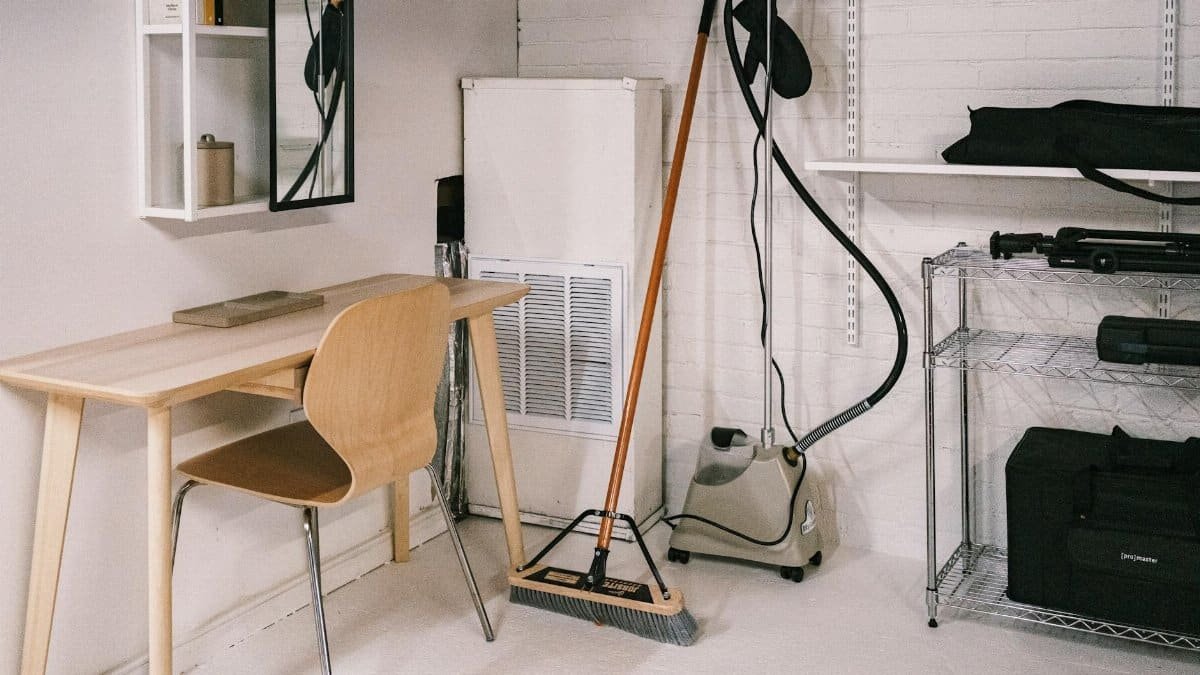 A tidy home office space featuring a wooden desk, chair, broom, and cleaning equipment.