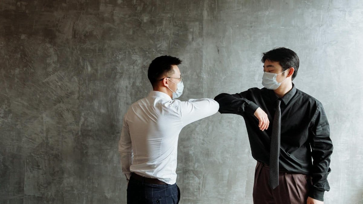 Two masked professionals greet with an elbow bump, following health protocols.