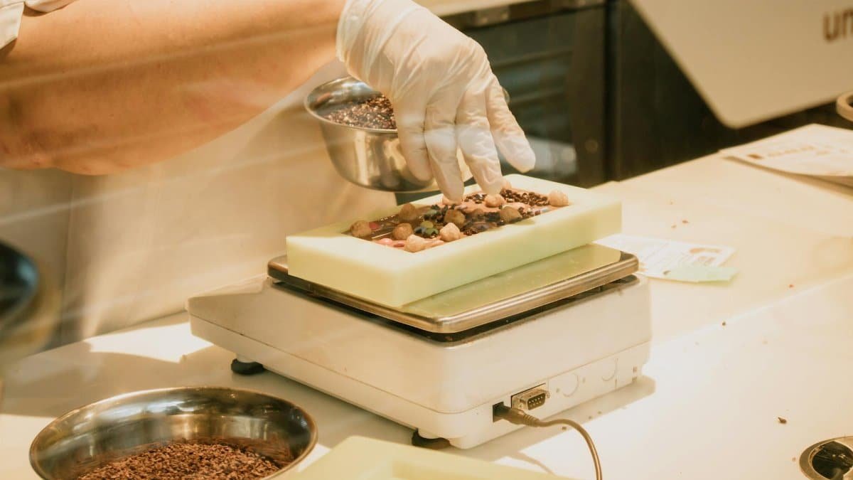 Chef in gloves arranging chocolate and ingredients on a kitchen scale for confectionery preparation.