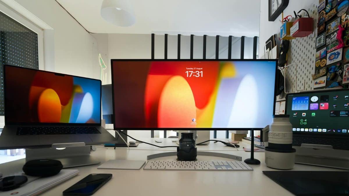 A sleek home office setup featuring multiple screens, laptops, and camera lenses on a white desk.