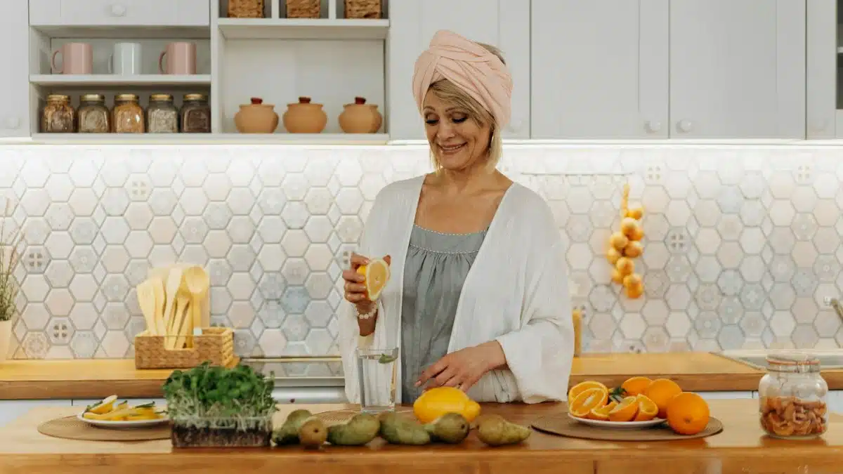 Smiling woman squeezing orange in a modern kitchen setting, emphasizing citrus freshness and healthy lifestyle.