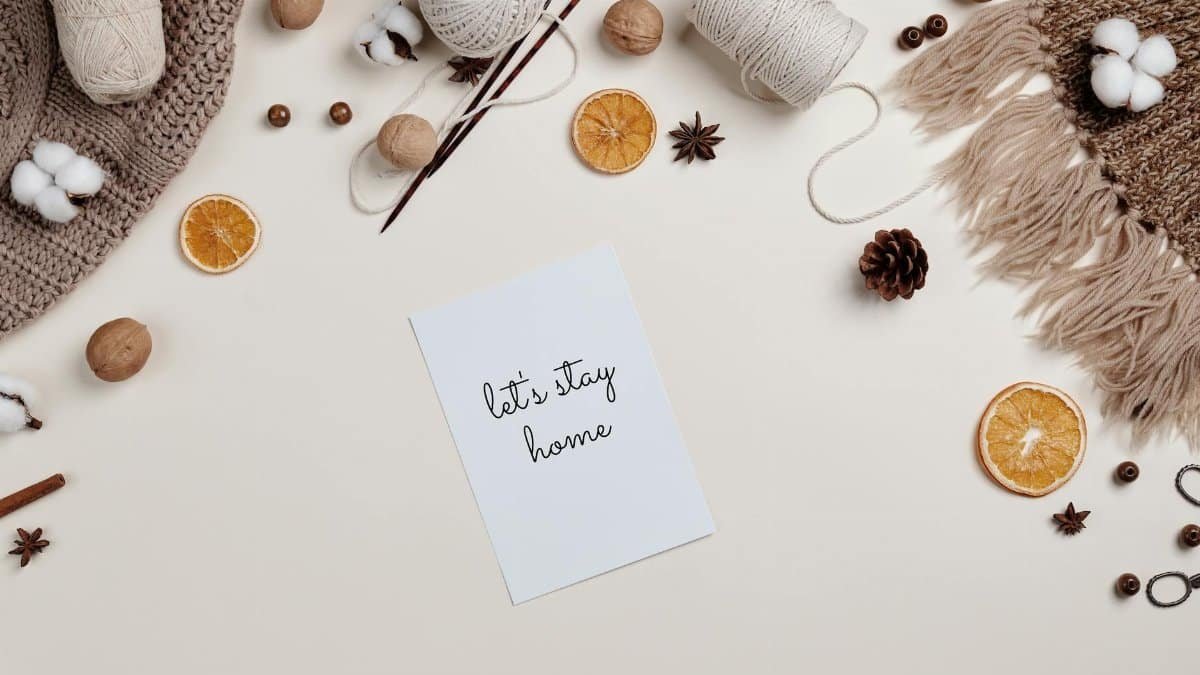 Flatlay of knitting materials, orange slices, and cozy decor with a 'Let's Stay Home' note.