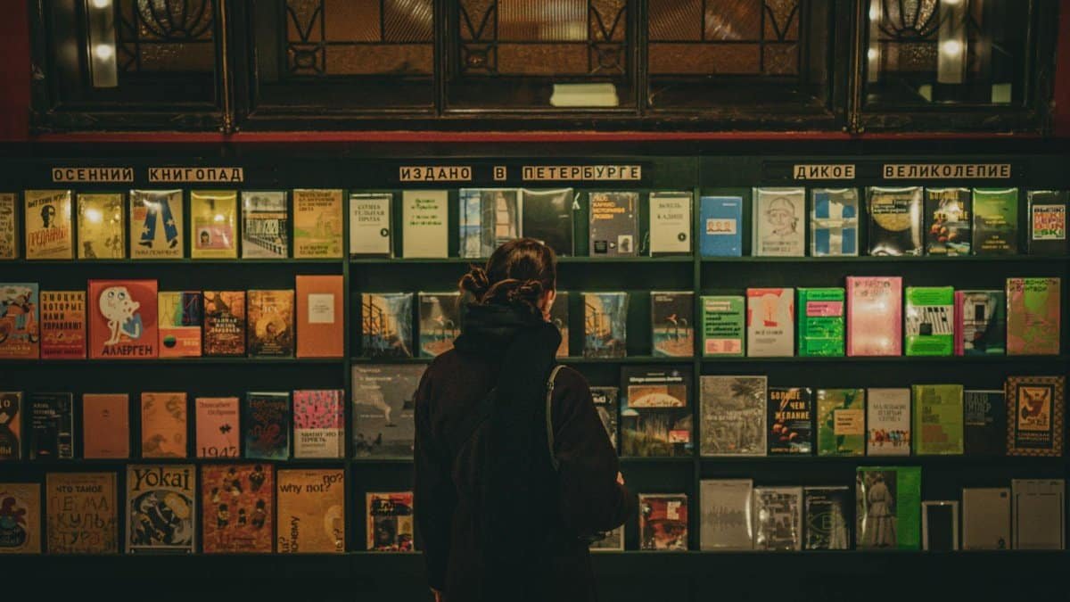 A woman selecting books from a well-lit shelf in a Saint Petersburg library.