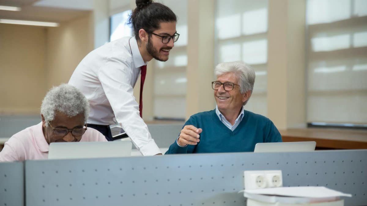 A classroom scene in Portugal where seniors learn computer skills from a young instructor. Engaged and smiling.