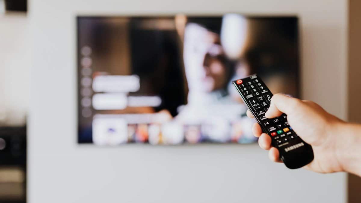 Person using a TV remote control with a blurred television screen in the background.