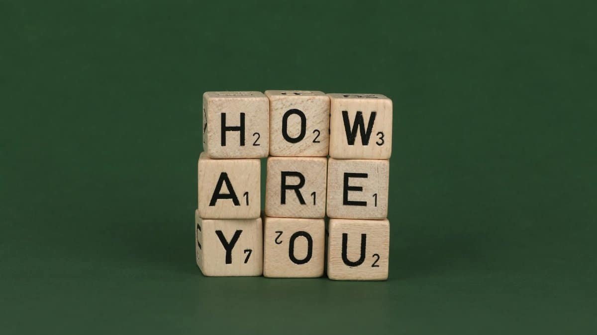 Wooden Scrabble letter blocks spelling 'how are you' on a green background.