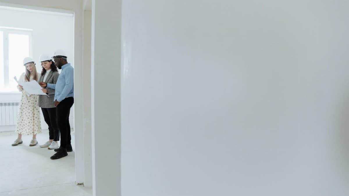 Architects wearing hard hats review blueprints inside a building under construction.