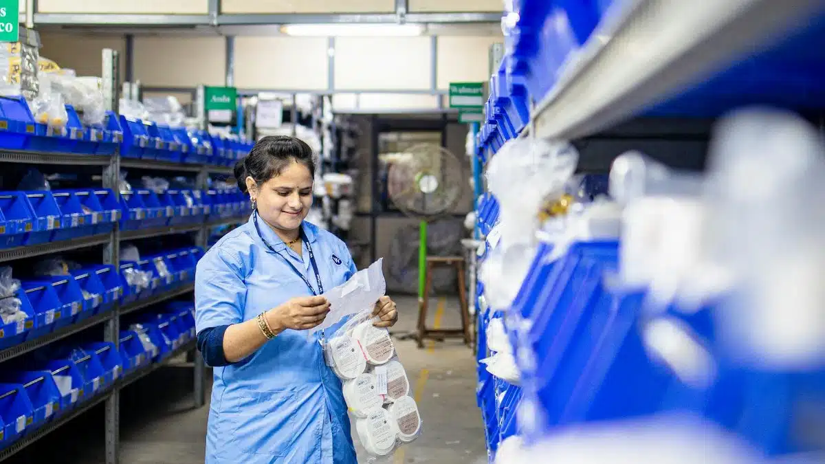 A woman in blue uniform organizing inventory in a warehouse aisle, focused on efficiency.