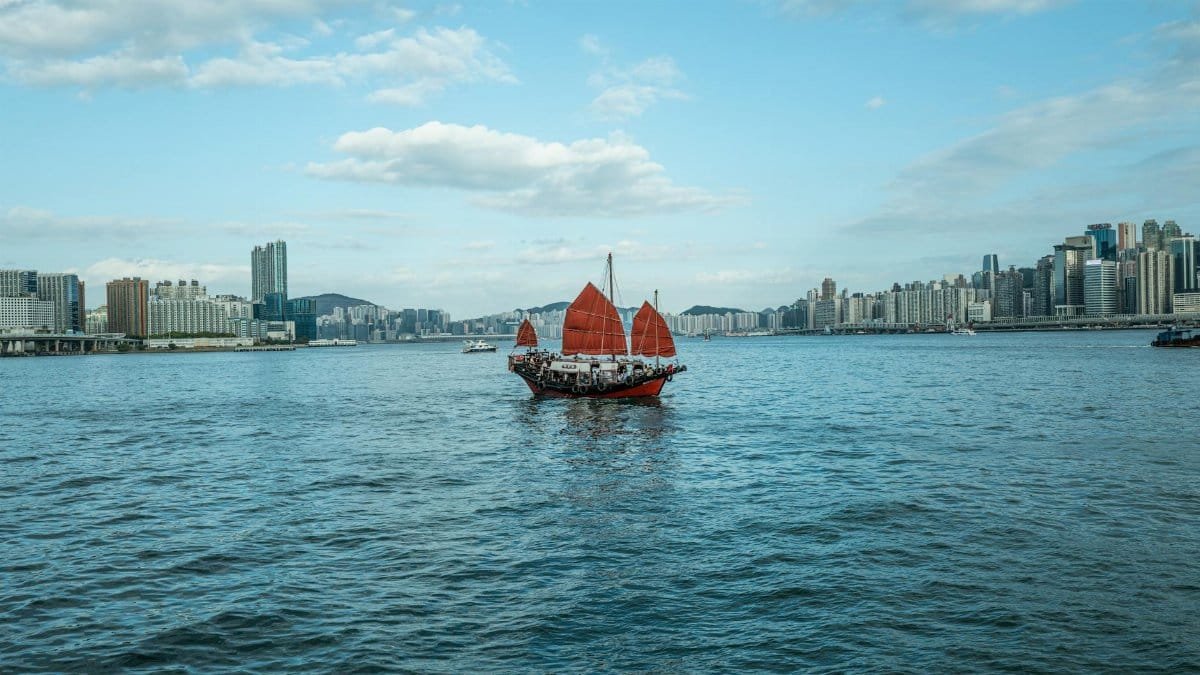 A traditional red-sail junk boat sails across the scenic Victoria Harbour in Hong Kong.