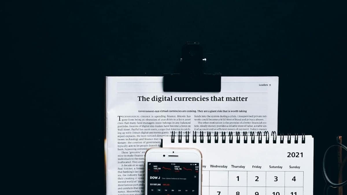 Digital currencies article with smartphone stock market app and calendar on black surface.