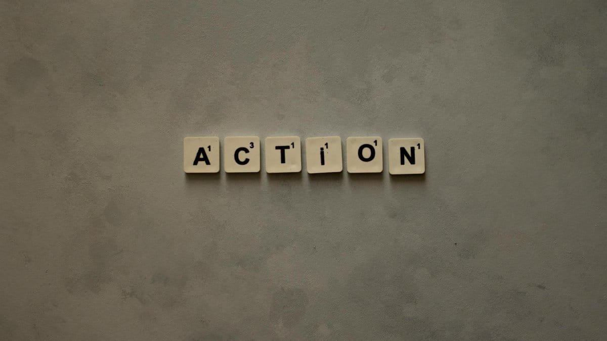 Scrabble tiles forming the word 'Action' on a textured gray surface, conveying motivation.