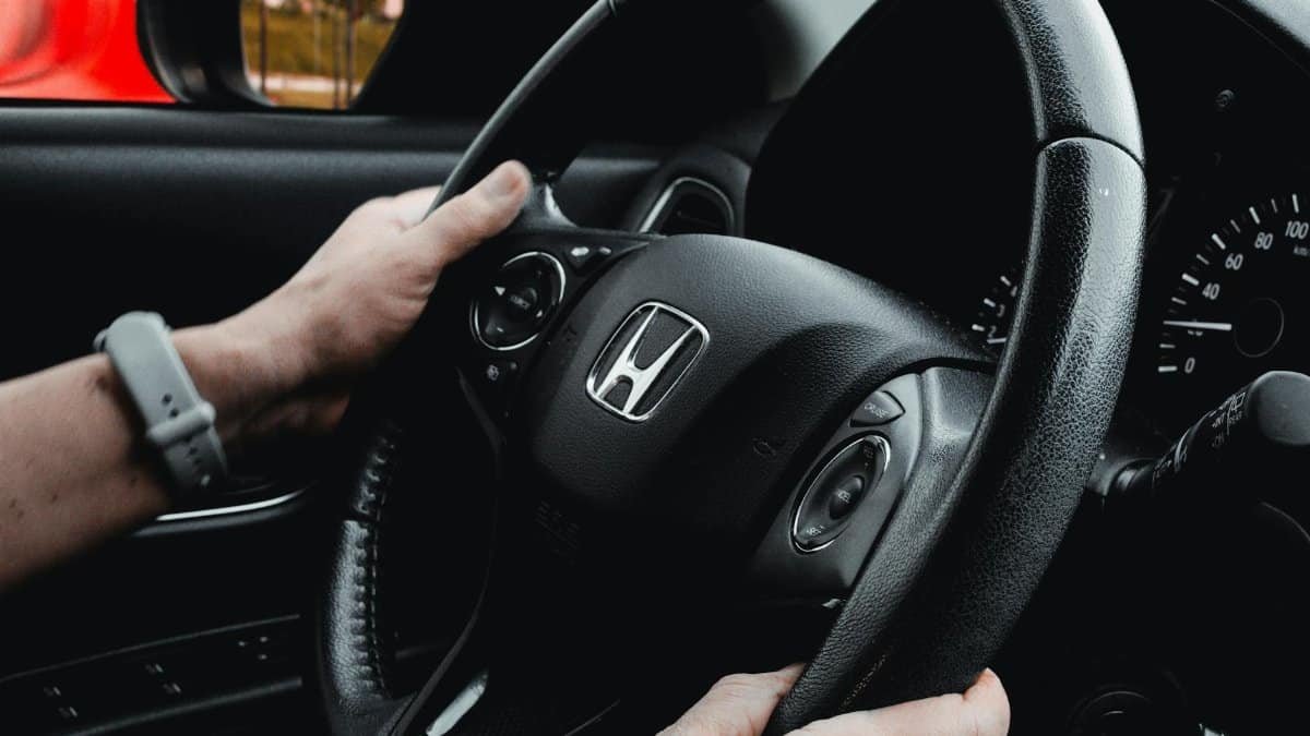 Close-up of hands holding a steering wheel inside a car, showing vehicle dashboard and controls.