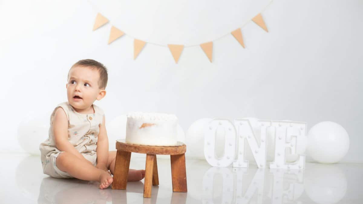 Adorable baby sitting by a birthday cake with a festive decoration celebrating the first birthday.