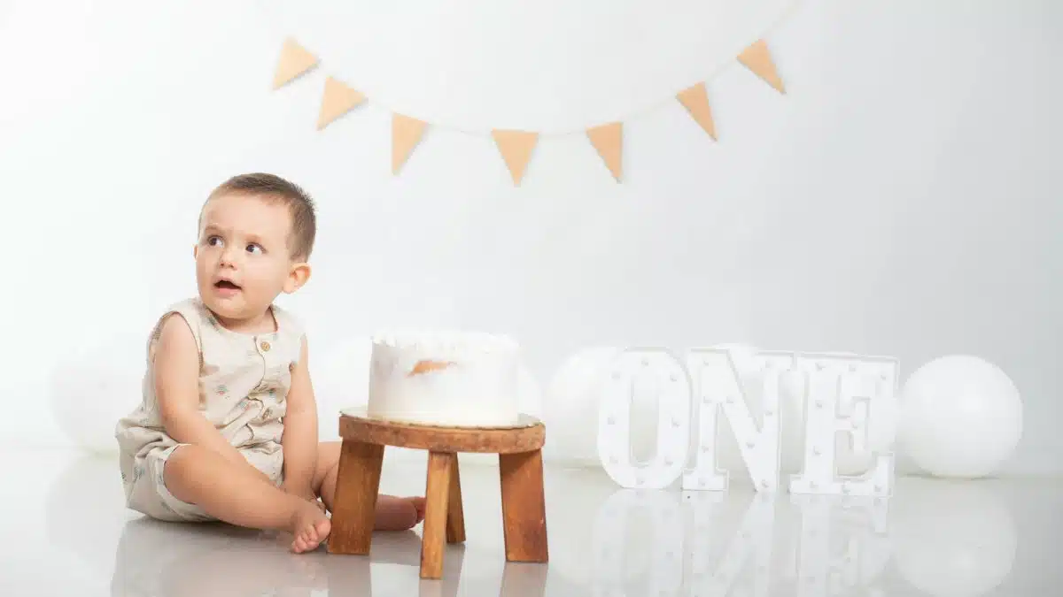Adorable baby sitting by a birthday cake with a festive decoration celebrating the first birthday.