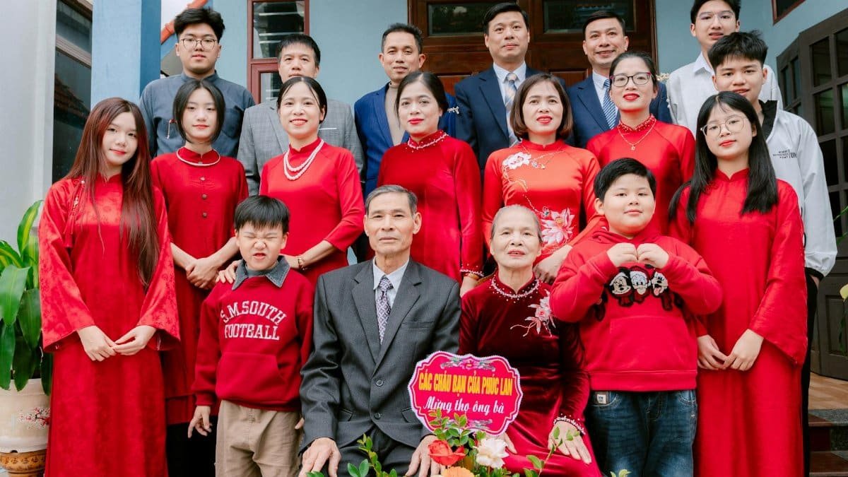 Large family gathering wearing traditional red outfits for a celebration, posing outdoors.