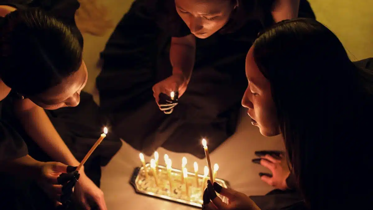 Top view of women holding candles in a dimly lit ritual setting, evoking spiritual themes.
