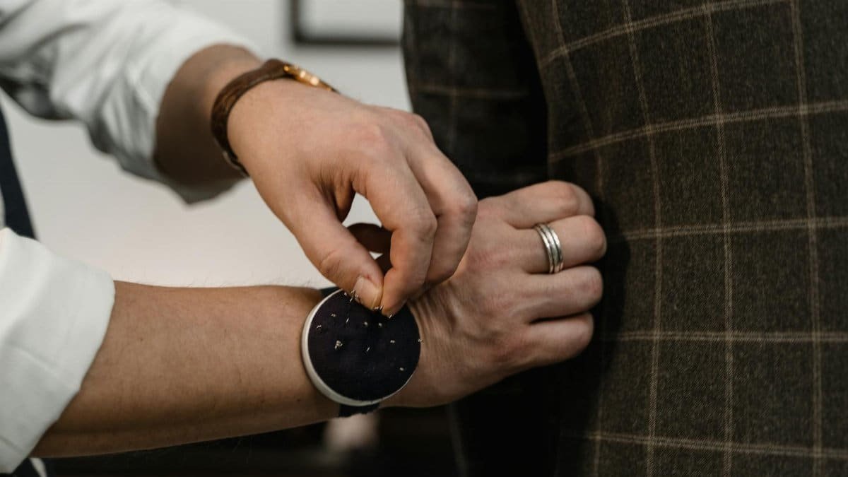 Close-up of a tailor adjusting a checkered suit jacket during a fitting session.