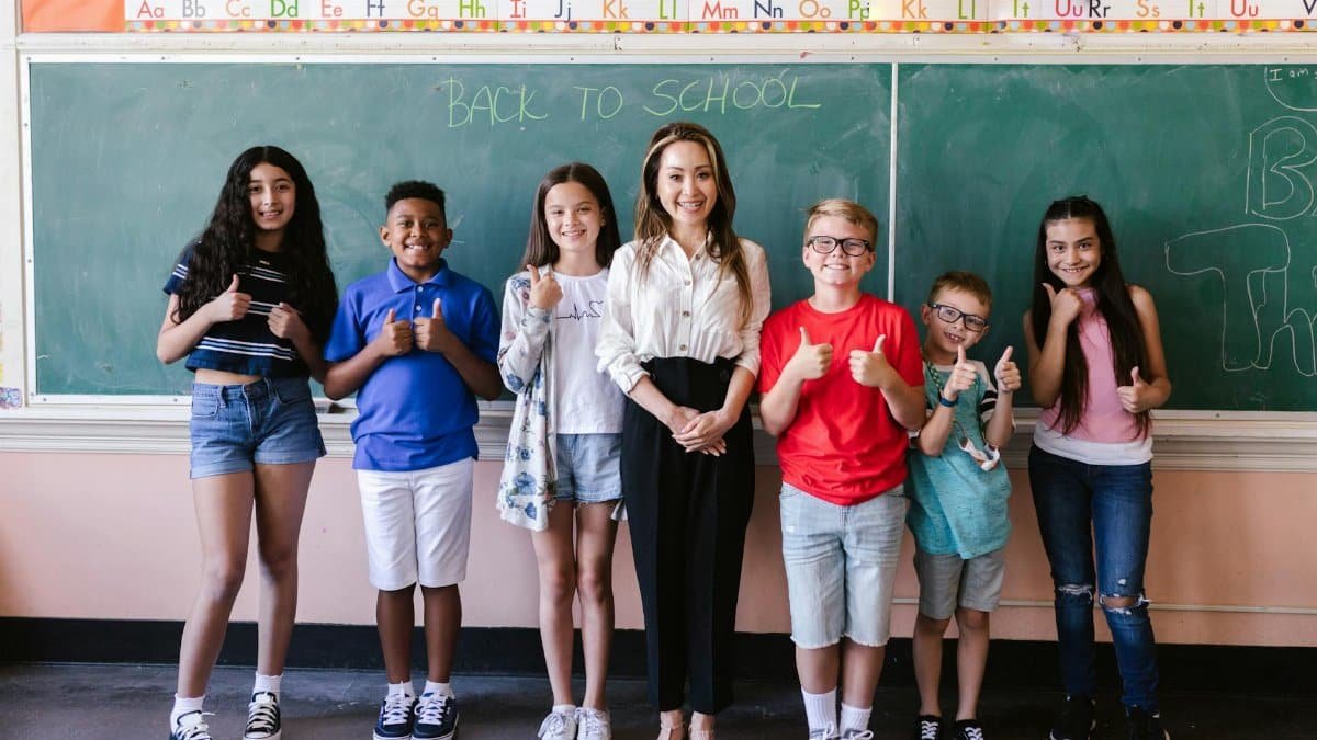 A diverse group of students and a teacher stand smiling in front of a back-to-school chalkboard.