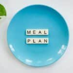Innovative meal planning concept using alphabet tiles on a blue plate with green leaves.