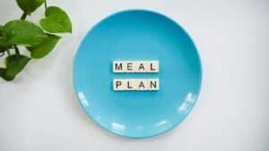 Innovative meal planning concept using alphabet tiles on a blue plate with green leaves.