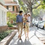 Family of three walking happily on a sunny day, enjoying urban scenery and nature.