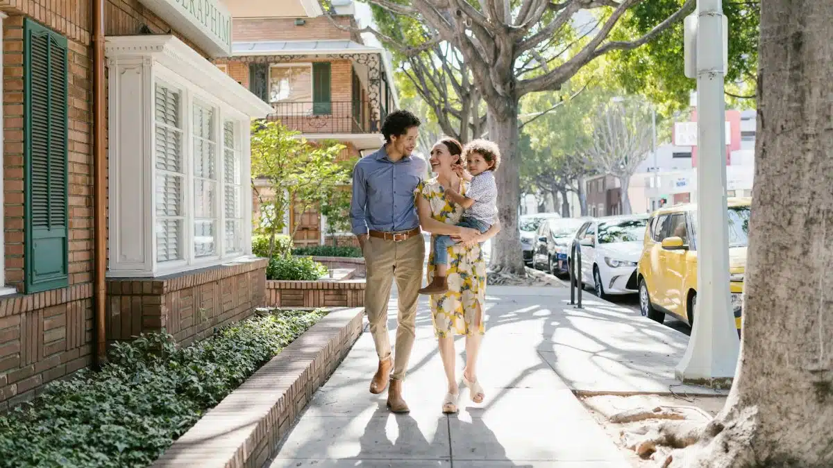 Family of three walking happily on a sunny day, enjoying urban scenery and nature.