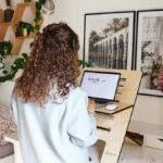 Woman using a laptop at home office standing desk with decor and laptop.