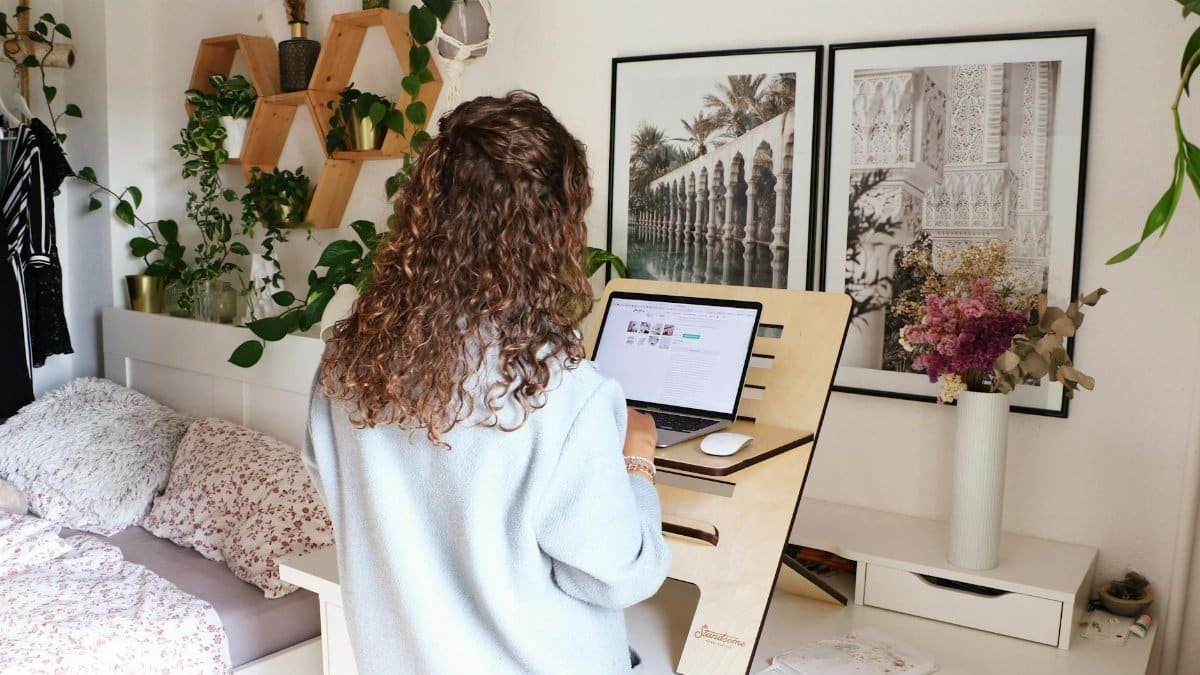 Woman using a laptop at home office standing desk with decor and laptop.