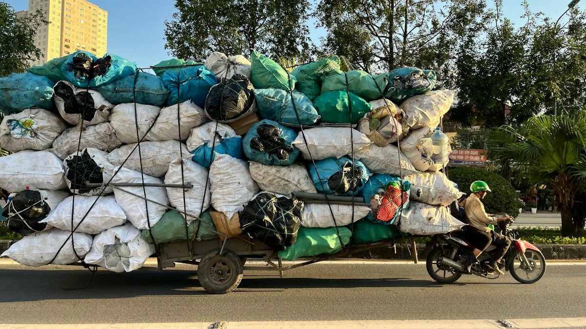 Motorbike overloaded with colorful cargo bags on a sunny street with green helmeted rider.