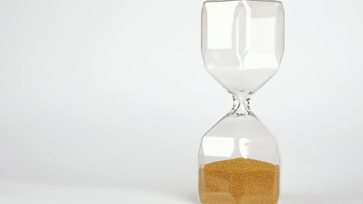 Transparent hourglass with golden sand symbolizing time and patience on a white background.