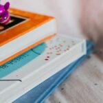 Close-up of colorful children's books stacked with a playful toy on top indoors.