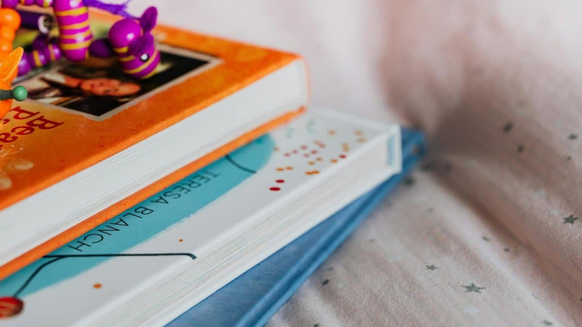 Close-up of colorful children's books stacked with a playful toy on top indoors.