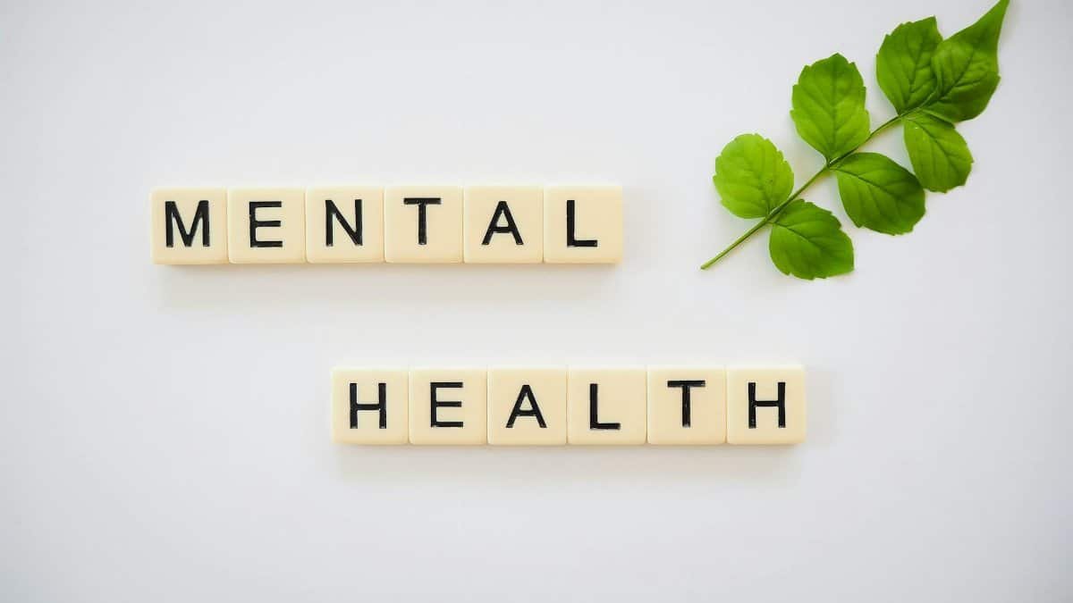 Scrabble tiles spelling 'Mental Health' with green leaves on a white background.