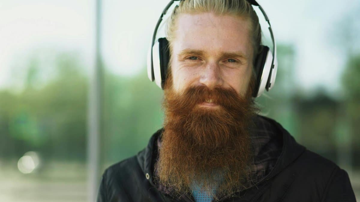 A man with a long red beard and headphones listening to music outdoors.