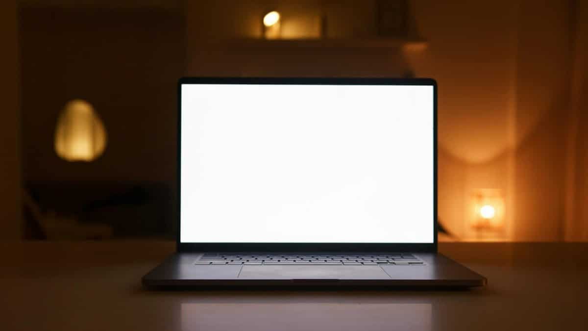 Laptop with a blank white screen on a desk in a warmly lit room, perfect for mockups or presentations.